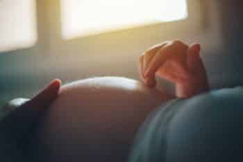 Pregnant woman cuddling belly in bedroom at home