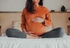 Pregnant woman sitting in crossed legs in be at home holding her belly