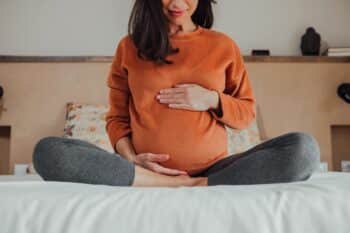 Pregnant woman sitting in crossed legs in be at home holding her belly
