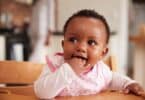 Cute Baby Girl Wearing Bib Sitting In High Chair