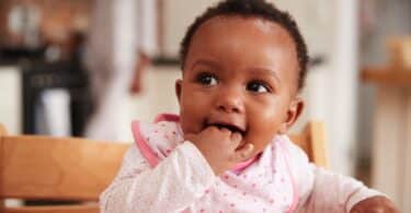 Cute Baby Girl Wearing Bib Sitting In High Chair