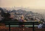 View Of Girl Looking At Cityscape While Sitting On Bench Against Clear Sky