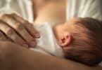 Newborn baby girl breast feeding in mothers arms