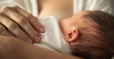 Newborn baby girl breast feeding in mothers arms