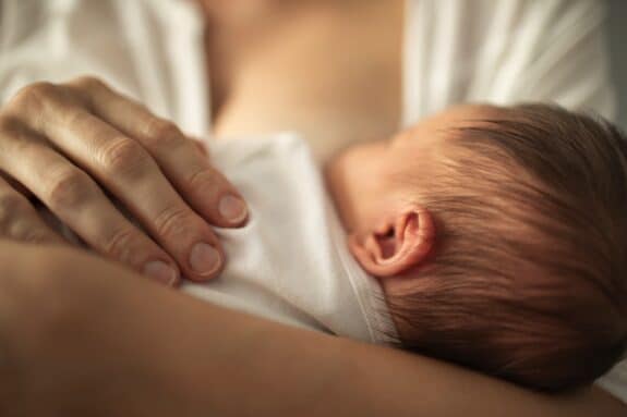 Newborn baby girl breast feeding in mothers arms