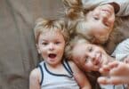 Portrait of three children lying on the bed. Sisters and brother smiling while looking at the camera