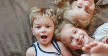 Portrait of three children lying on the bed. Sisters and brother smiling while looking at the camera