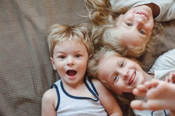 Portrait of three children lying on the bed. Sisters and brother smiling while looking at the camera